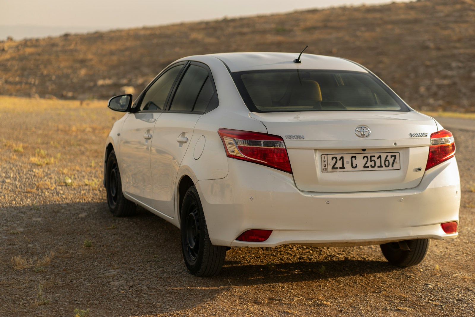 A white toyota sedan parked on a dirt road.