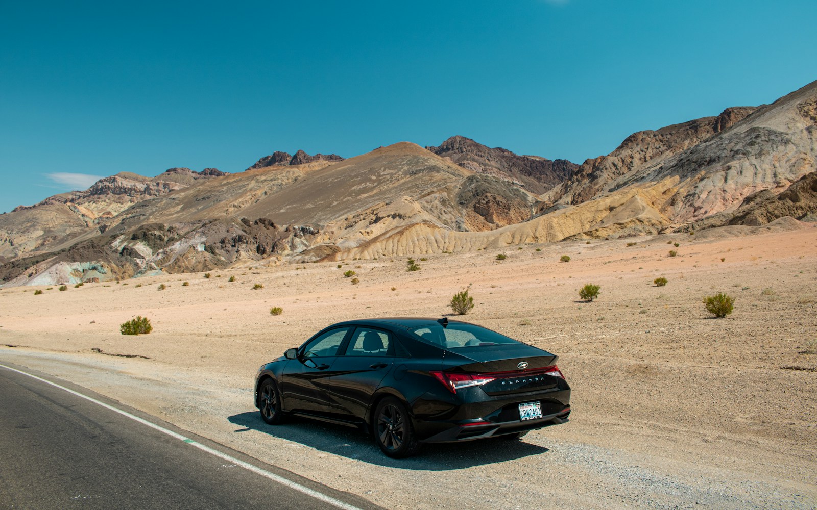 A black car driving down a desert road