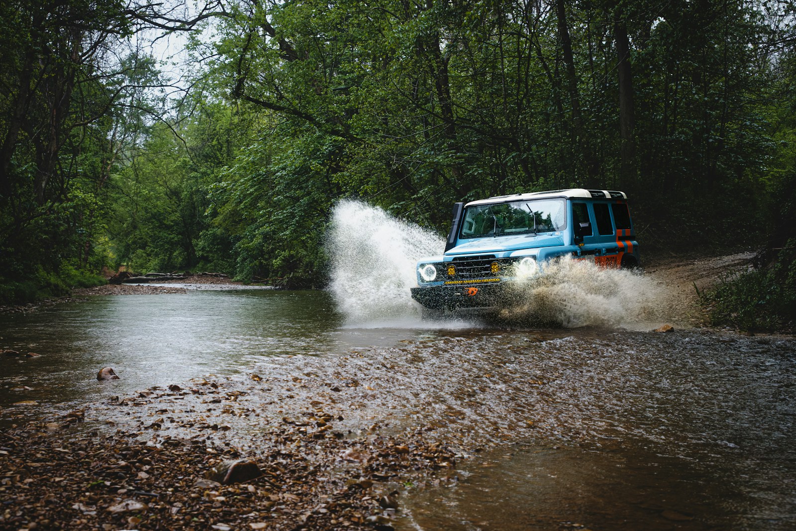 A car drives through a stream, making a splash.